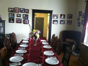 The dining table at the Dorothy Day House is often set for many people, as members of the community often visit for dinner. The walls are lined with pictures of the families that have stayed there.